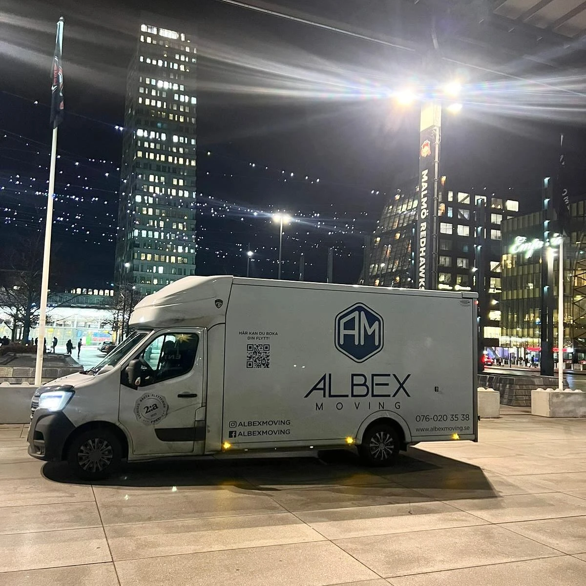 En vit flyttbil från Albex Moving parkerad utanför Malmö Arena i Hyllie, Malmö, under kvällstid med Point Hyllie i bakgrunden.